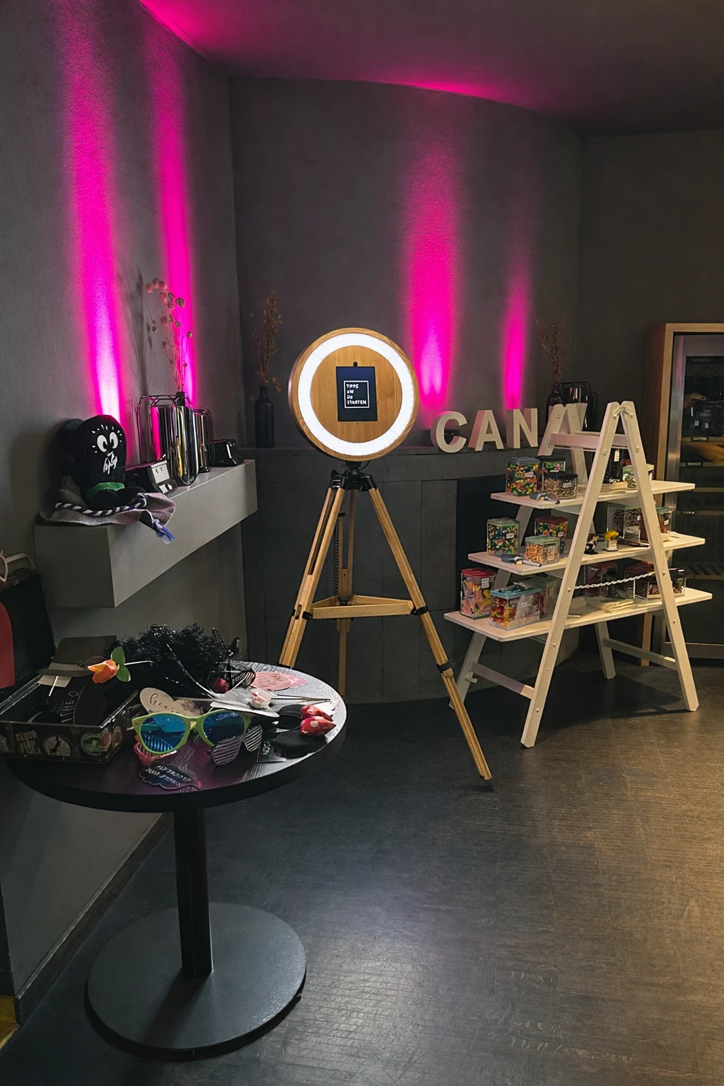 Moderne Fotobox mit Ringlicht auf Holzstativ bei einem Event-Setup von DJ Dirk, mit pinker Ambientebeleuchtung, Requisiten und Candybar im Hintergrund